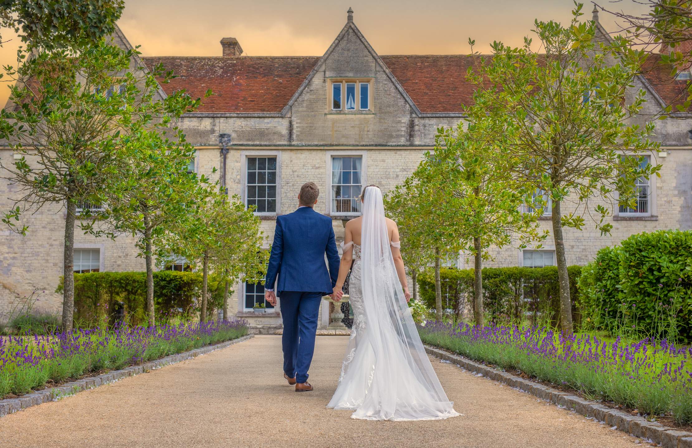 A couple walking down the grand tree lined entrance at Froyle Park, an exclusive use wedding venue in Hampshire