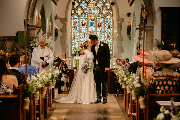 A Bride & Groom kiss after their church wedding ceremony at St Mary's in Hampshire, before heading to Froyle Park wedding venue next door for their wedding celebrations.