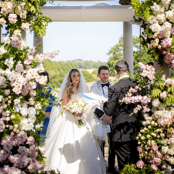 A Jewish bride and groom beneath their outdoor Chuppah begin their wedding ceremony