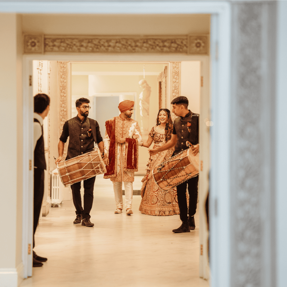 A beautiful Sikh Bride & Groom entering their wedding reception with Dhol drummers at Froyle Park - an exclusive use wedding venue in Surrey specialising in dry hire Asian weddings.