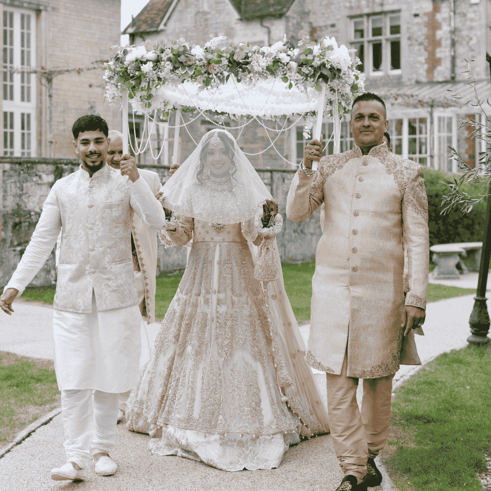 A Bride being escorted to her outdoor Muslim Nikkah ceremony by her brother and father under a canopy at Froyle Park - a wedding venue in Surrey specialising in Asian weddings.