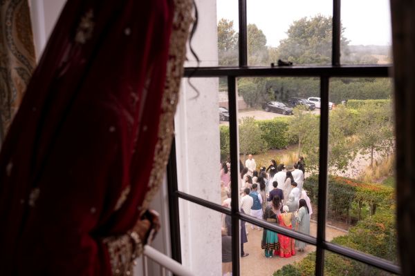 A Bride peeks from the upsatirs window as her guests arrive at Froyle Park
